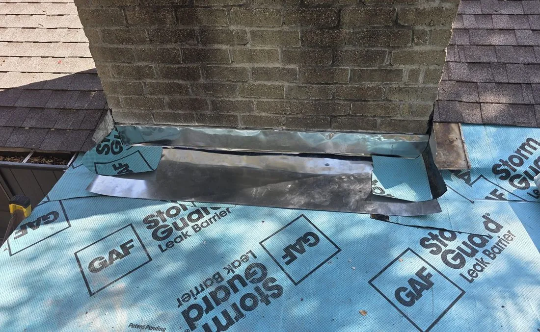 Chimney flashing in progress over blue self-adhered leak barrier on a Central Texas reroof, apron and step pieces visible