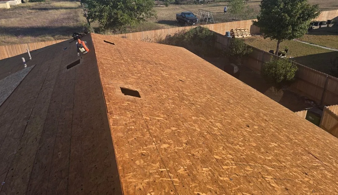 Roof deck at tear-off with OSB panels, vent openings cut and old decking on the far roof plane