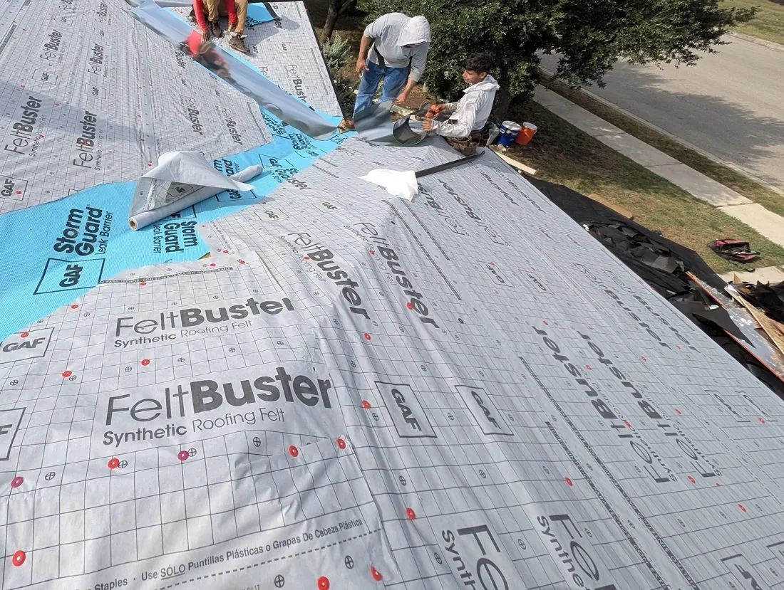 Gray synthetic underlayment with printed fastener marks across a roof, with blue leak barrier in a valley