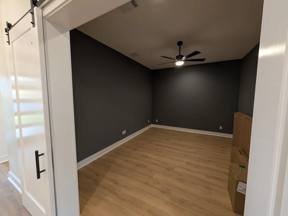 Room with a dark accent wall, white trim and a ceiling fan