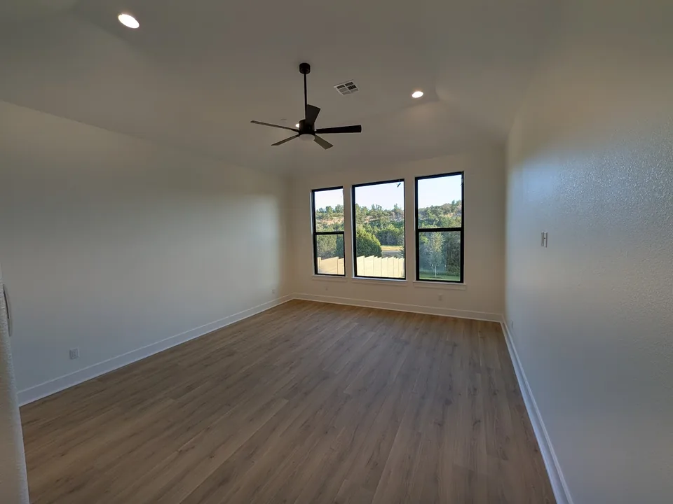 Empty room with light painted walls, three windows and a ceiling fan