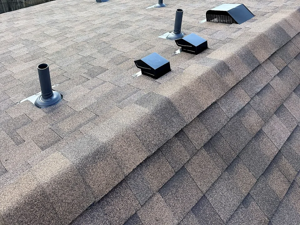 Box vents and pipe flashings in a row just below the ridge cap of a shingle roof