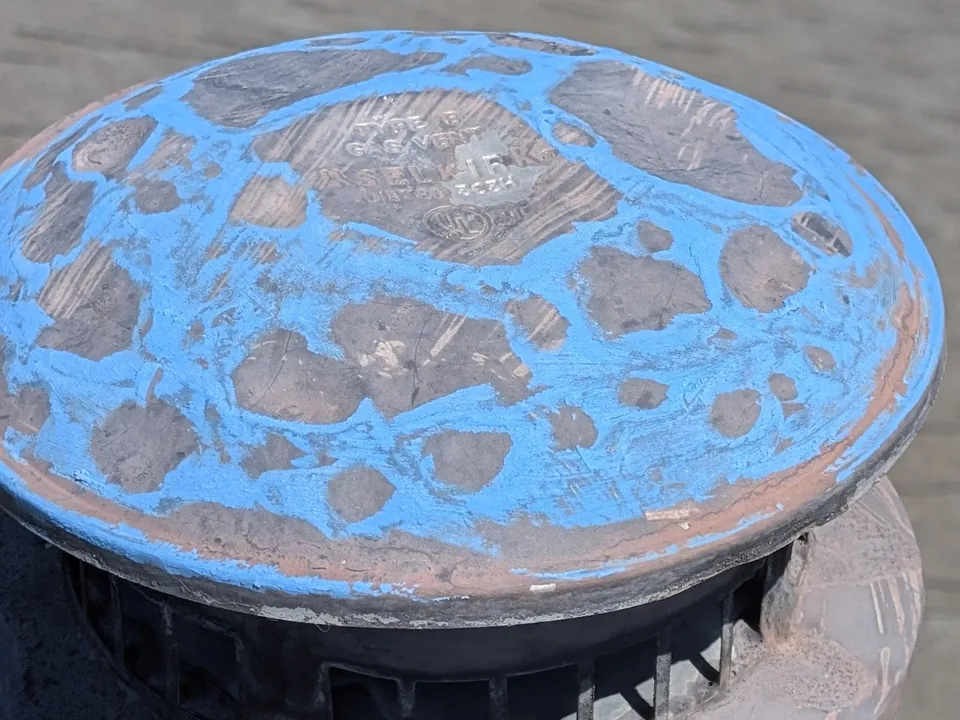 Close view of a dented metal vent cap rubbed with blue chalk
