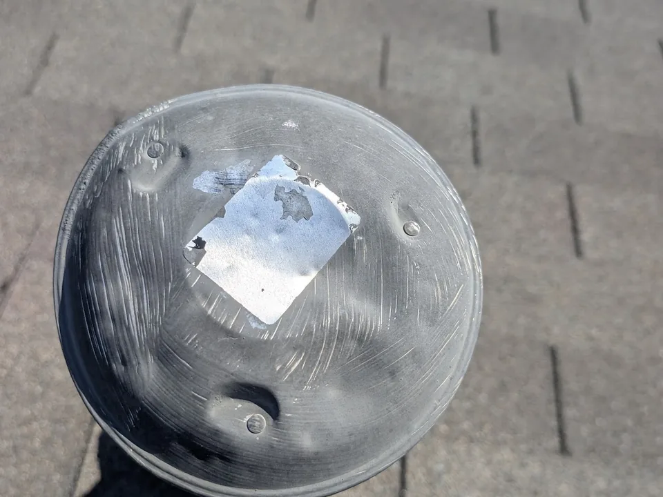 Dented round vent cap on a shingle roof with a foil tape patch