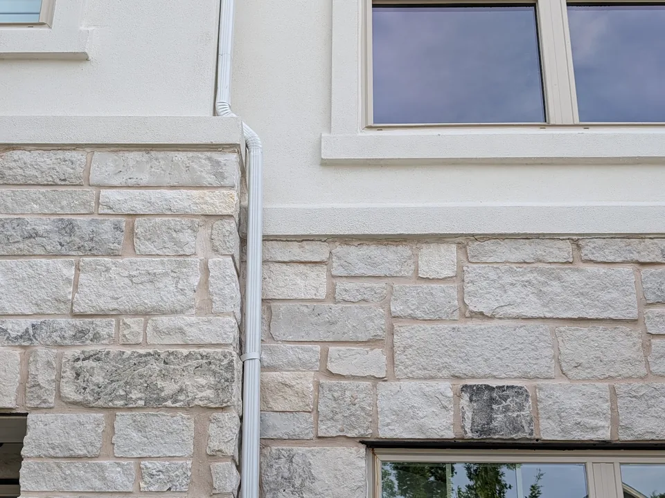 White downspout running down a stone and stucco wall