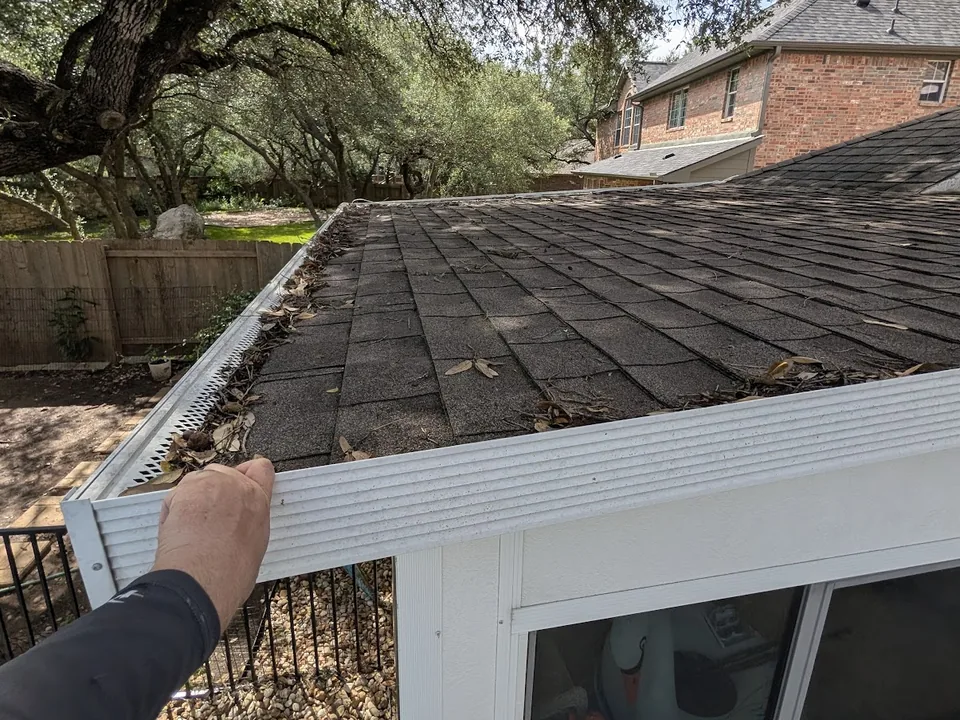 Hand lifting a gutter guard with leaves and debris at the roof edge
