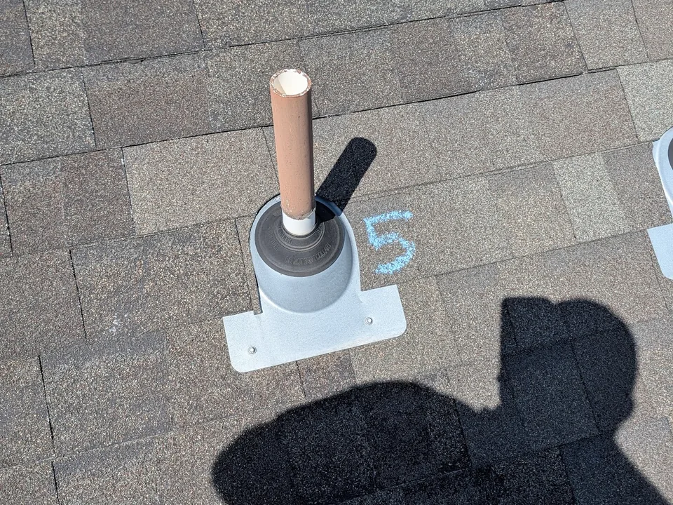 Plumbing vent boot on a shingle roof with a chalk number beside it
