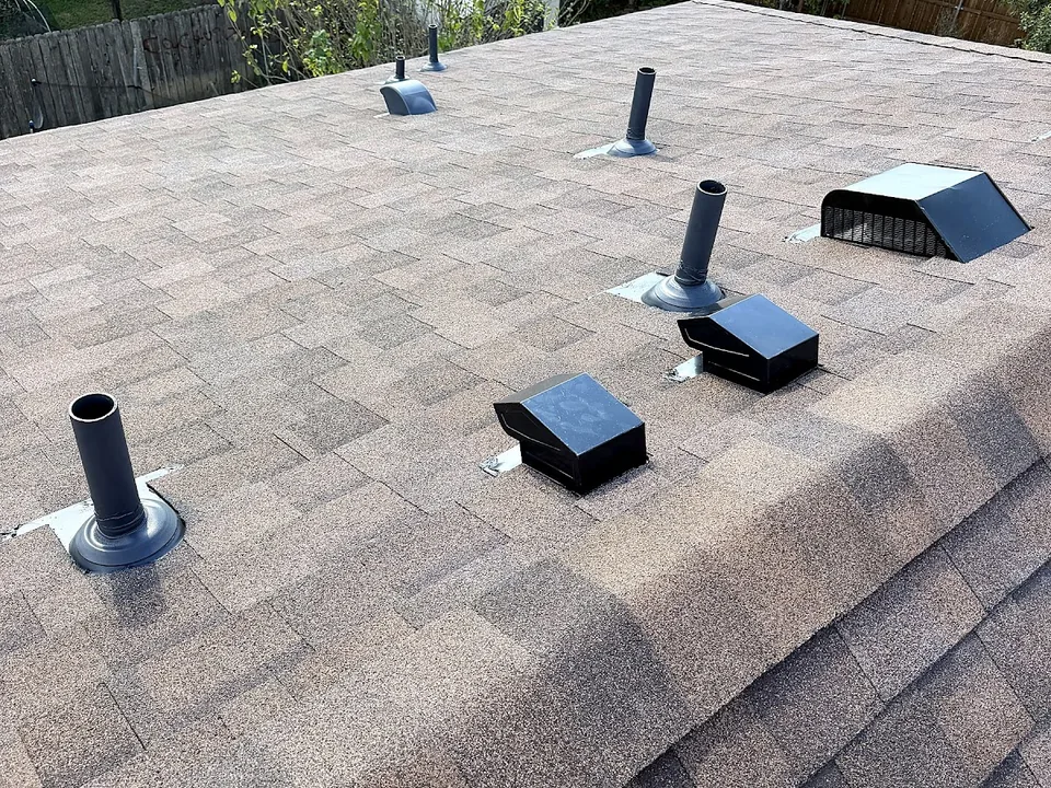 Pipe flashings and box vents set into the shingles just below a ridge cap