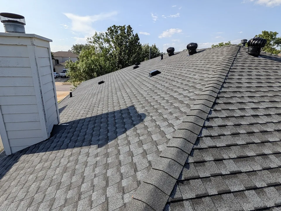 Shingle roof meeting a sided chimney chase, with vents along the ridge
