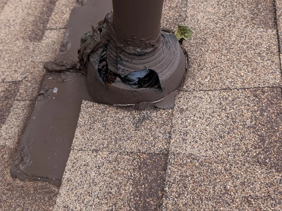 Cracked plumbing vent boot on a shingle roof smeared with sealant