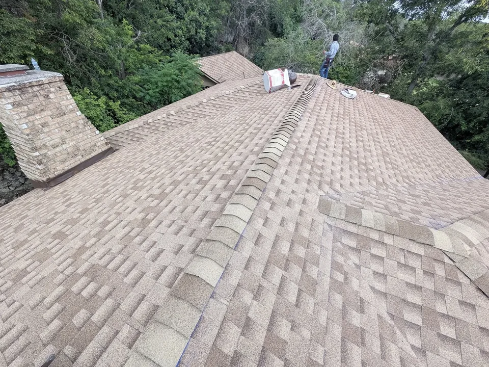 A tan shingle roof with its ridge cap and chimney