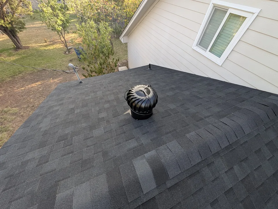Turbine vent on a charcoal shingle roof next to a sided wall